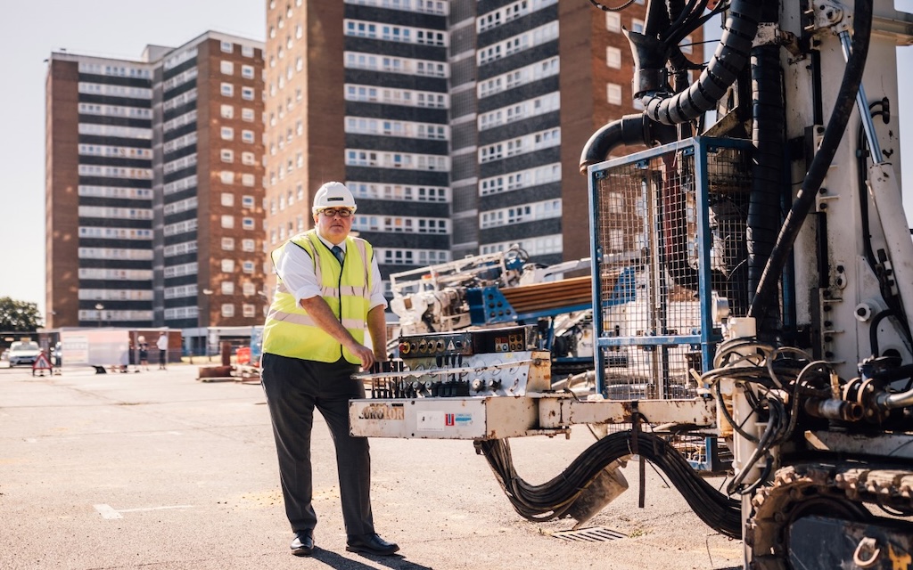 Photo of Cllr Gledhill standing in front of residential flats with machinery for installing heat pumps